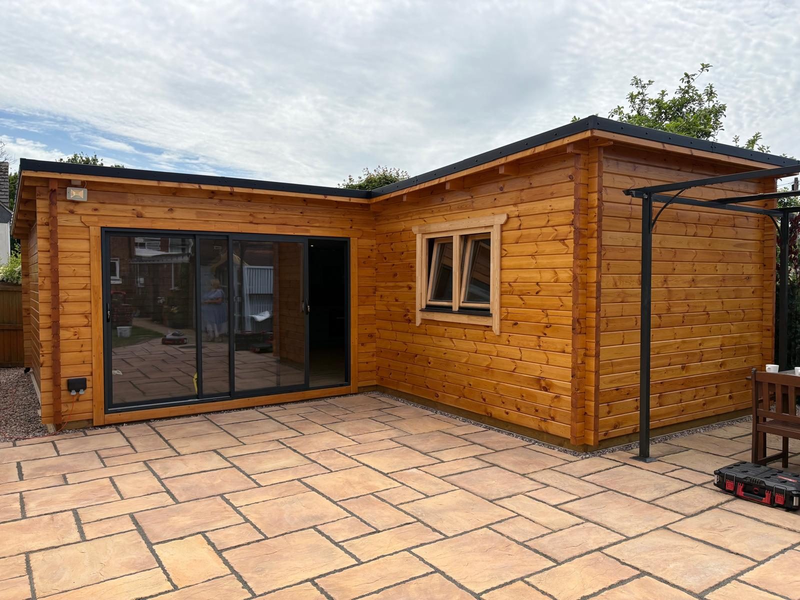 L-shaped log cabin with bifold doors and a pergola on a patio