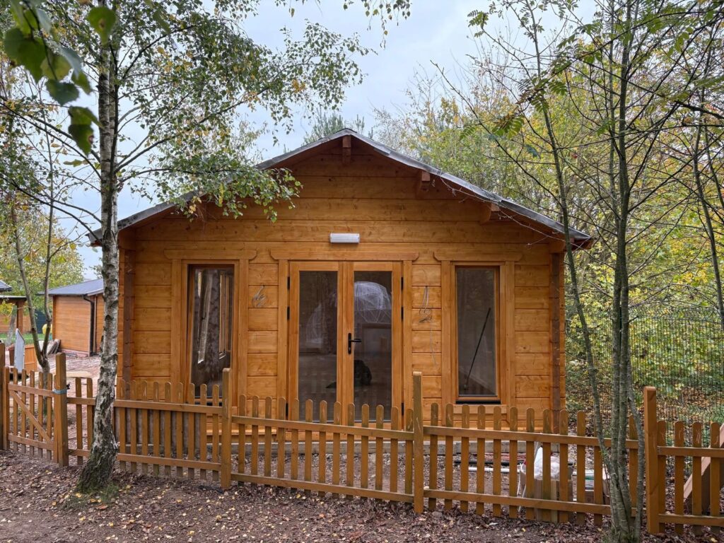 Stained apex log cabin with a picket fence and a glazed door